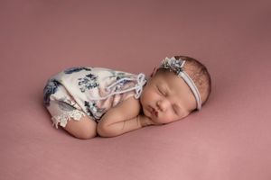 Sleeping newborn in floral outfit on pink background.
