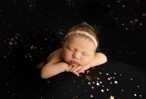 Sleeping newborn on black background with scattered gold star decorations.