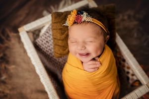 Happy newborn wrapped in mustard yellow swaddle with floral headband.