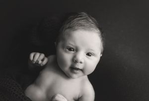 Black and white portrait of a baby with bright eyes and bare shoulders against dark background.