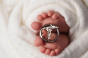 Diamond engagement ring balanced on tiny baby feet wrapped in white fabric.
