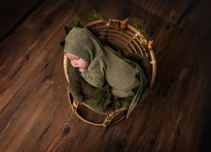 Tiny baby wrapped in olive green knit wrap sleeping in wooden basket.