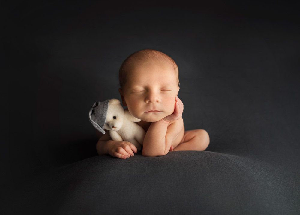 Sleeping newborn posed with white bunny against dark background.