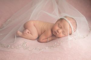 Newborn sleeping on pink tulle with delicate lace headband.