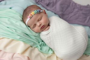 Sleeping newborn wrapped in white swaddle with turquoise headband on pastel bedding.