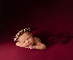 Sleeping newborn with floral headband on deep red background.