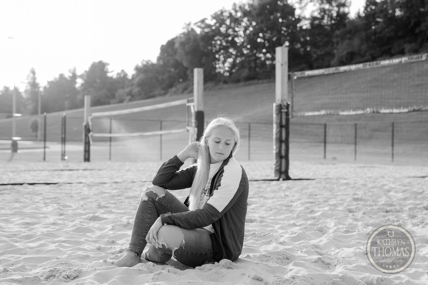 Black and white portrait of athlete sitting on volleyball court in casual pose.
