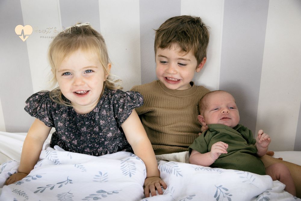 two kids with a baby in bed
