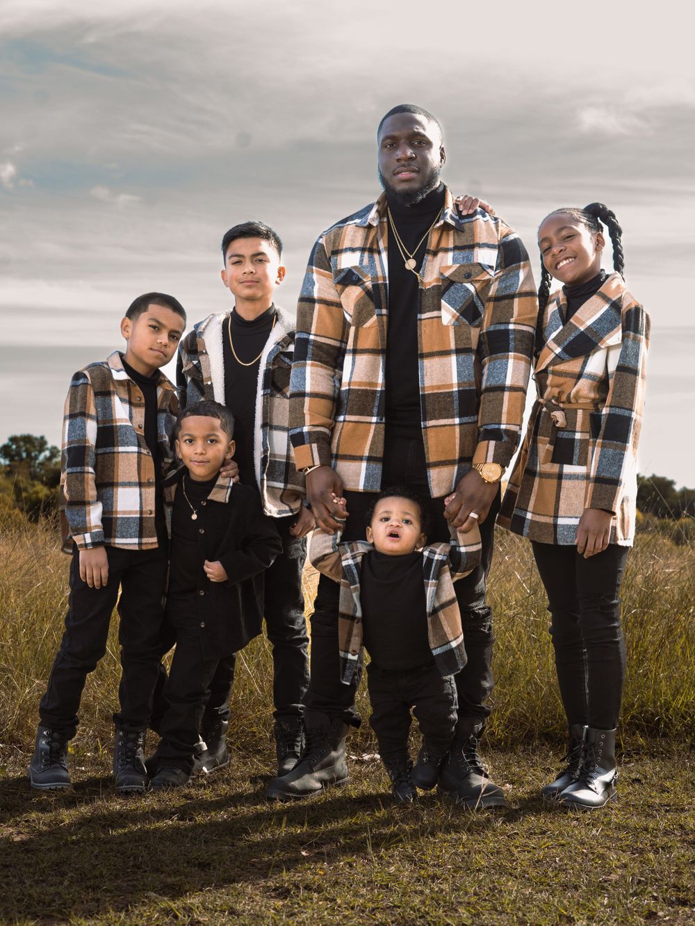 Group portrait in coordinating brown plaid jackets posing in a grassy field.