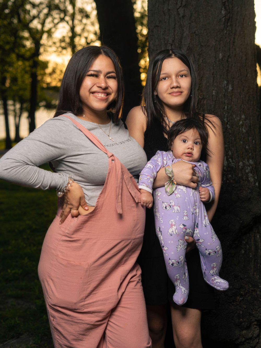 Family portrait with baby in purple onesie during sunset by trees.