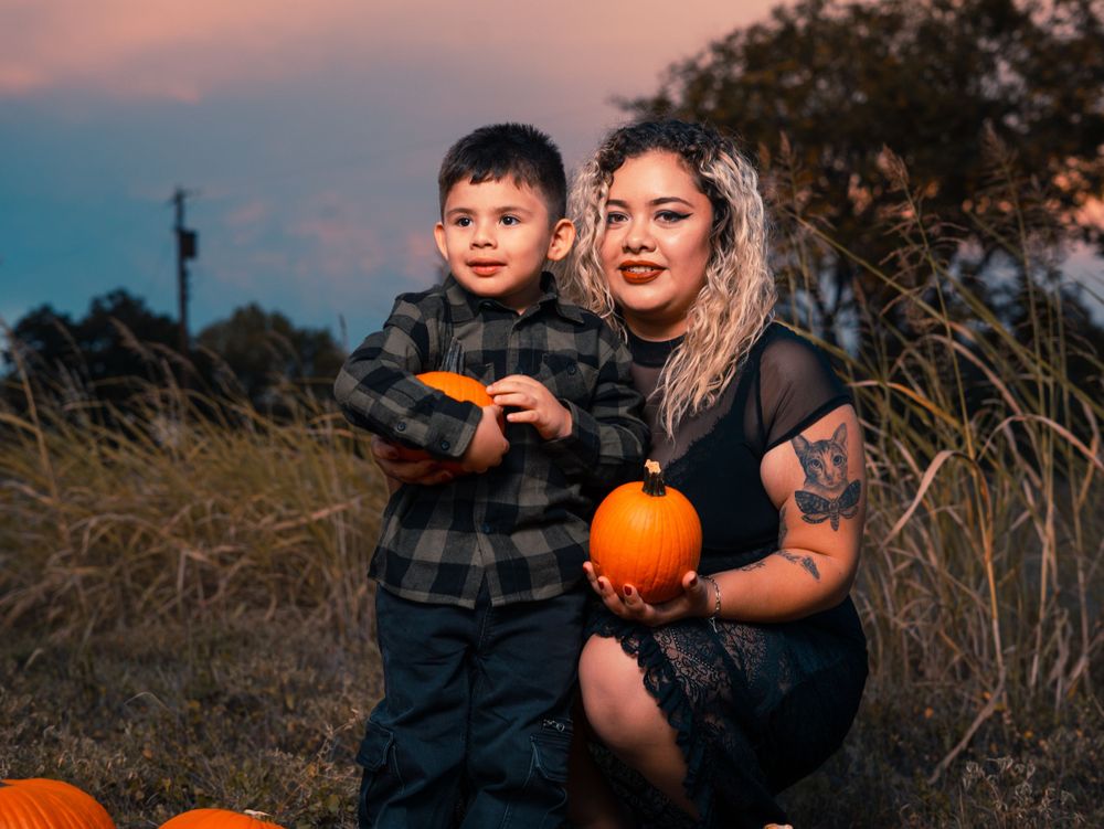 Mother and child holding pumpkin during autumn sunset photo session.