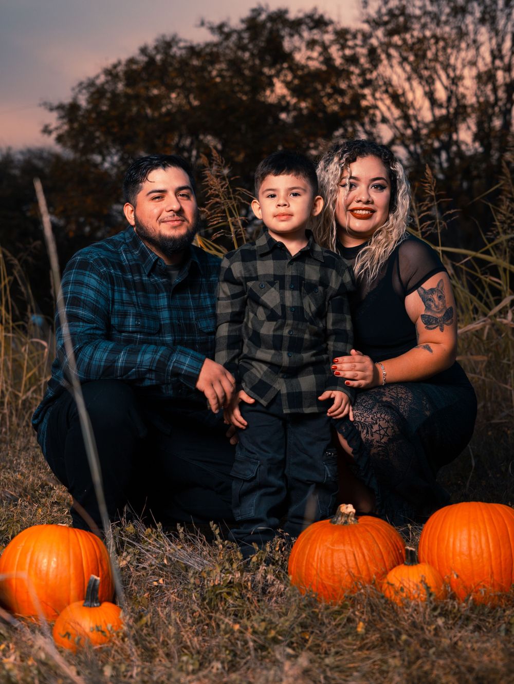 Family autumn portrait with pumpkins during sunset in tall grass field.