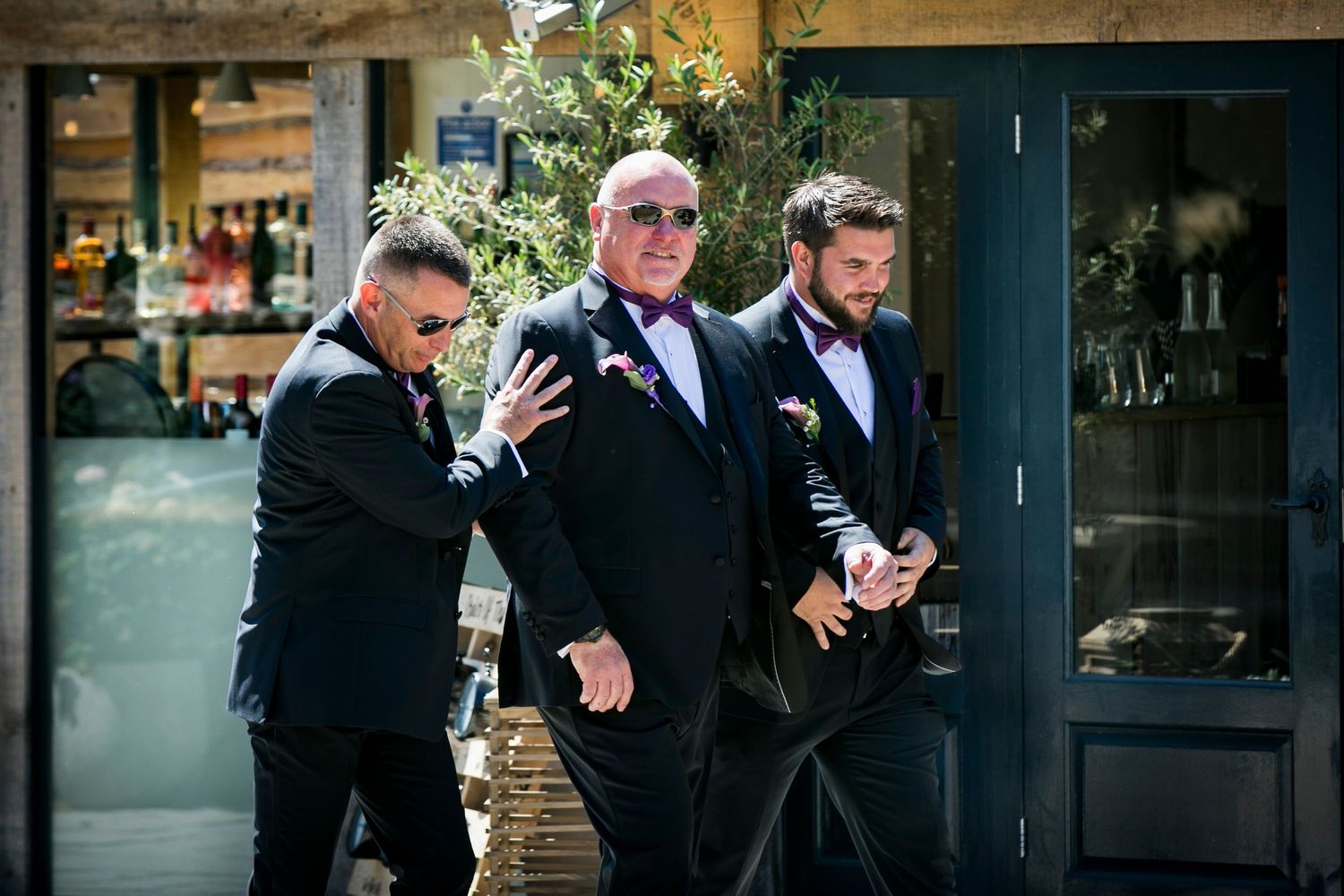 Groomsmen in dark suits posing casually outside a modern building.