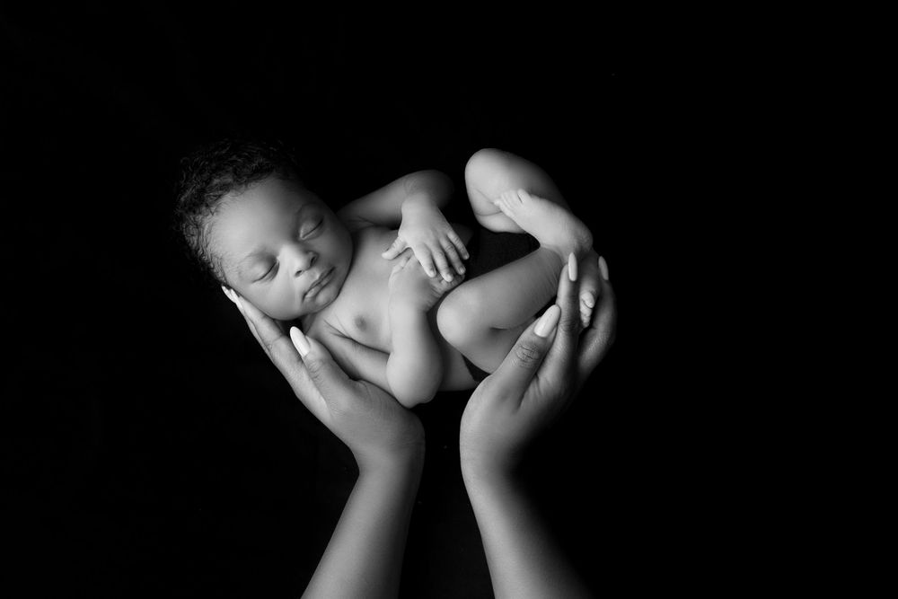 Artistic black and white portrait of sleeping newborn cradled in hands.