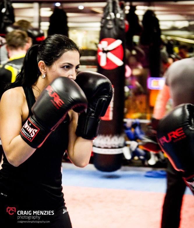 Female boxer wearing Twins boxing gloves sparring with a partner at Pure Fitness gym.