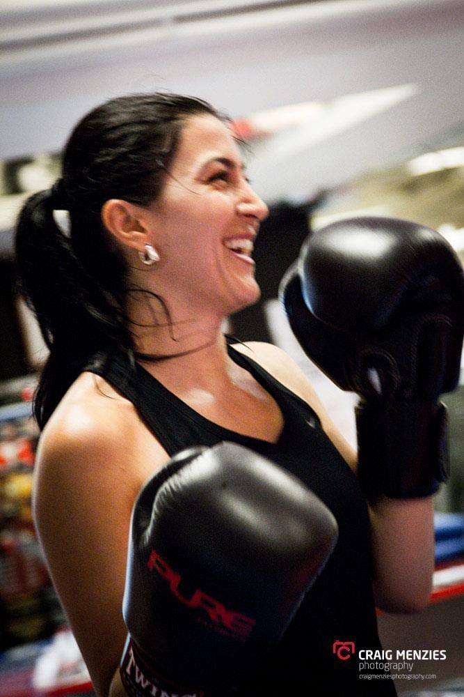 Smiling dark-haired woman in boxing gloves laughing during training session at boxing gym.