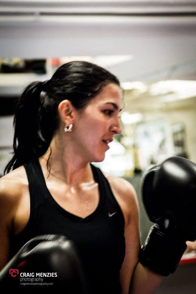 Close-up of focused female boxer with dark ponytail wearing black boxing gloves during training.