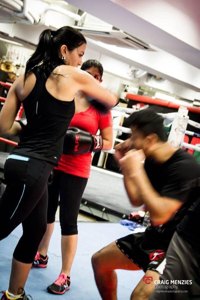 Female boxers training in a boxing ring with a male coach during gym workout session.