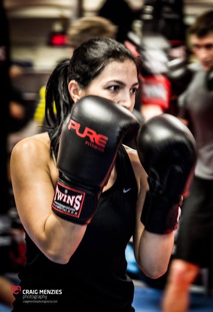 Female boxer in Pure Fitness Twins boxing gloves in fighting stance at indoor gym.