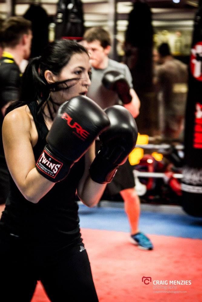 Female boxer wearing headgear and Twins boxing gloves in defensive stance at boxing gym.