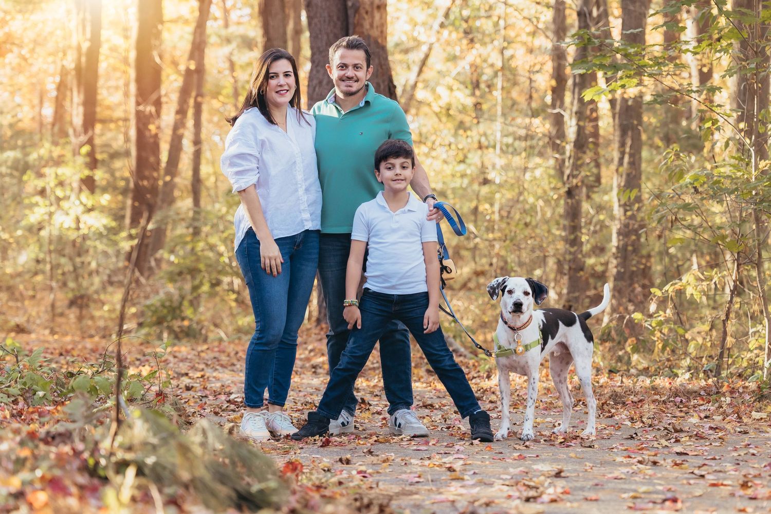 Family walking with their dog on an autumn trail through a sunlit forest.