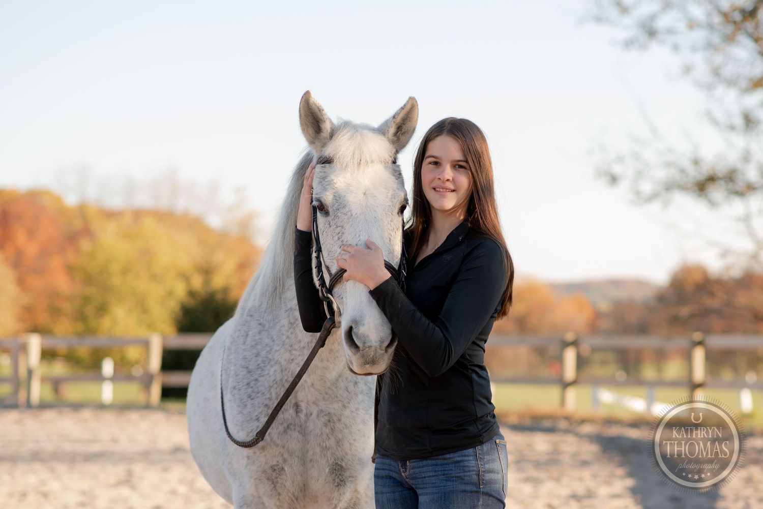 Person in black sweater embracing a white horse during autumn photo session.