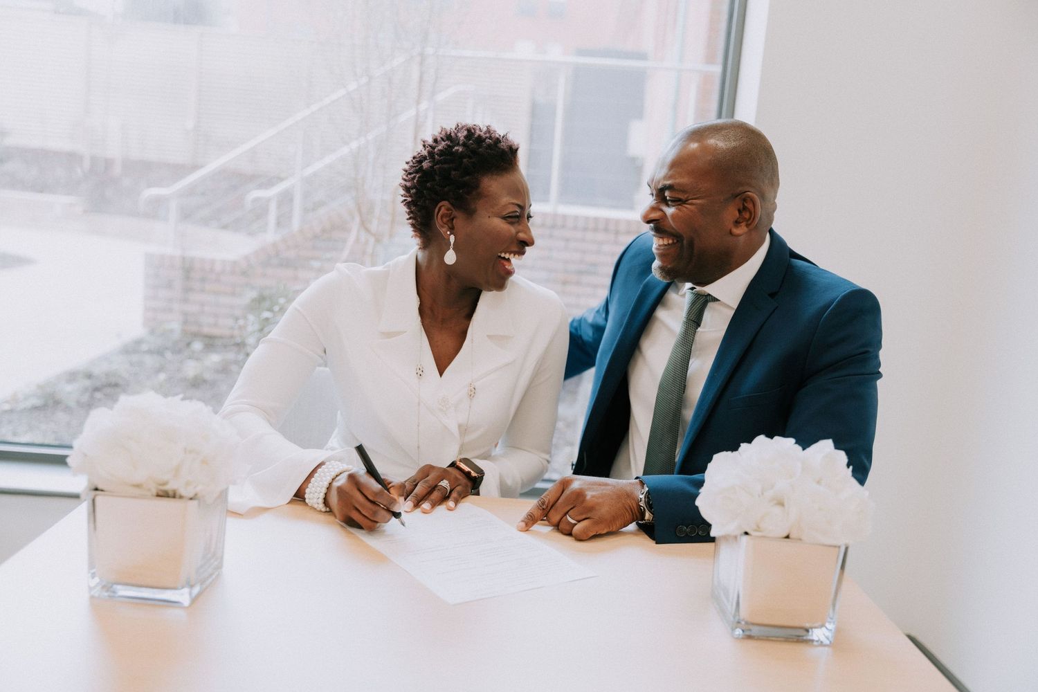 A couple exchanges warm glances while completing paperwork at a modern office table.