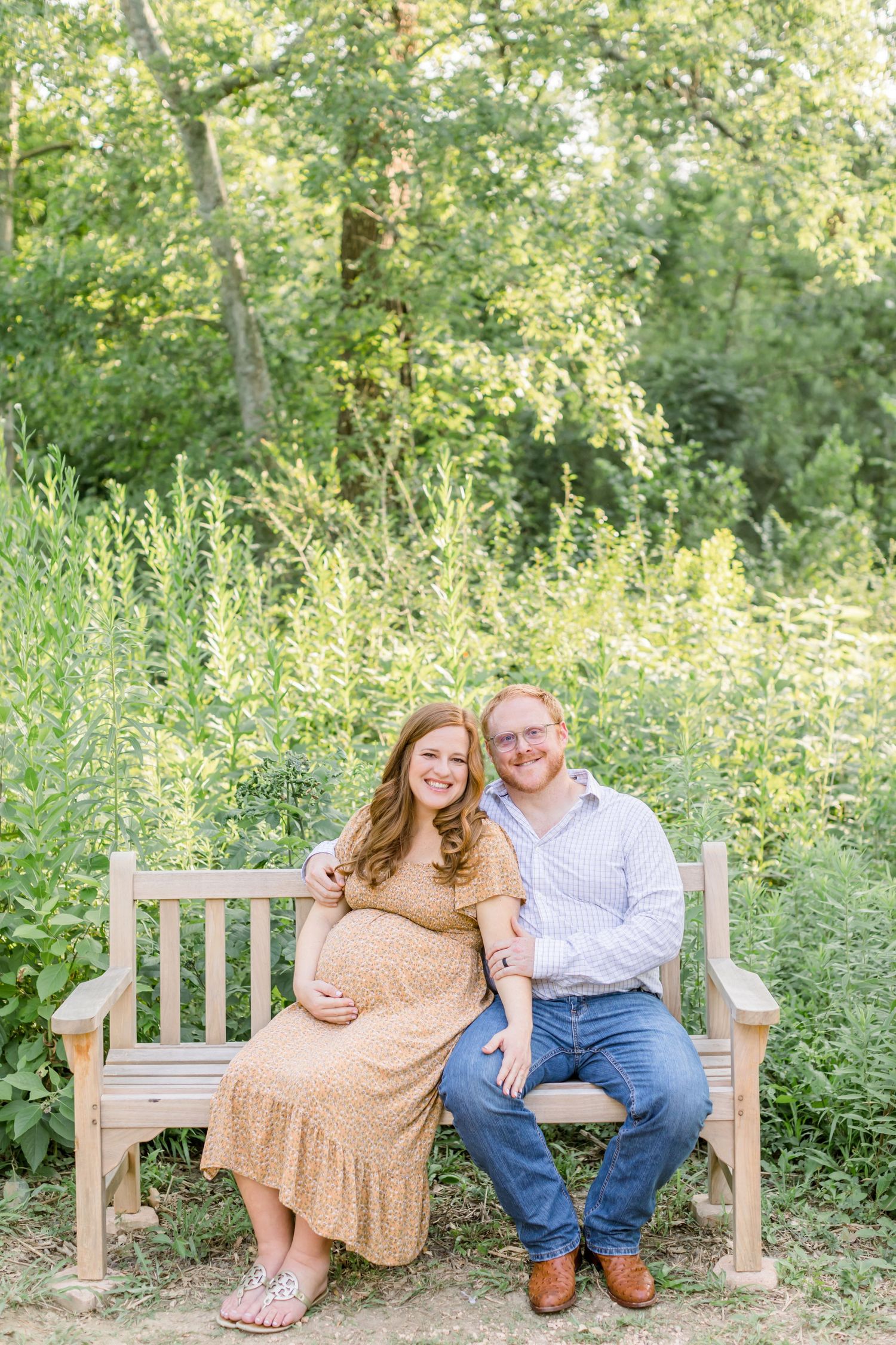 A couple sits together on wooden garden bench surrounded by blooming summer greenery.