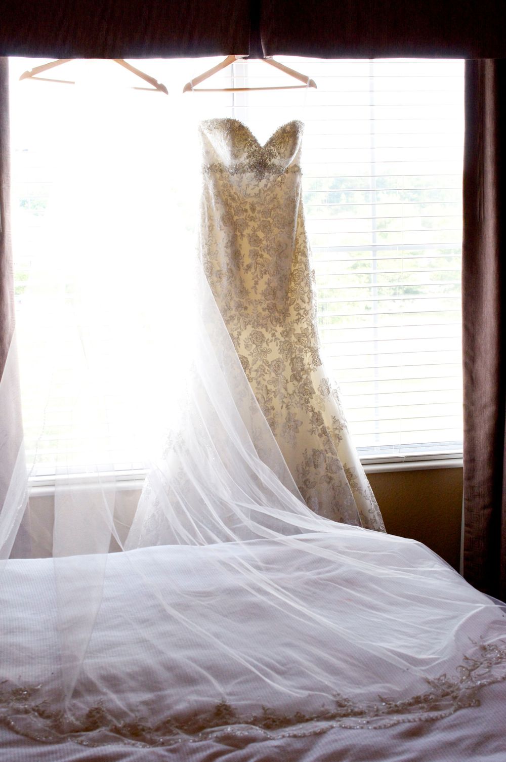 Wedding dresses on hangers displayed against window with flowing veils and lace details.