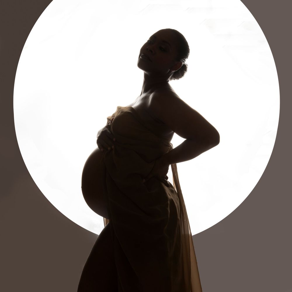 Pregnant NYC model photographed at June Photography Studio.  Model is posed infront of a round backlit light.  Silhouette of pregnant model.
