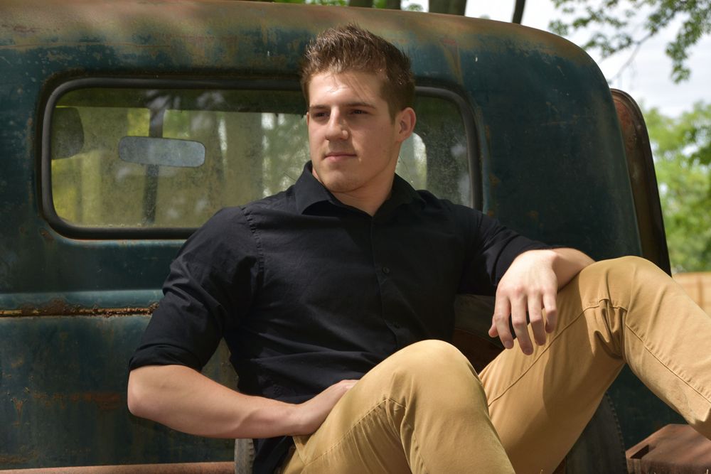 Person in black shirt reclines against vintage truck door in casual pose.