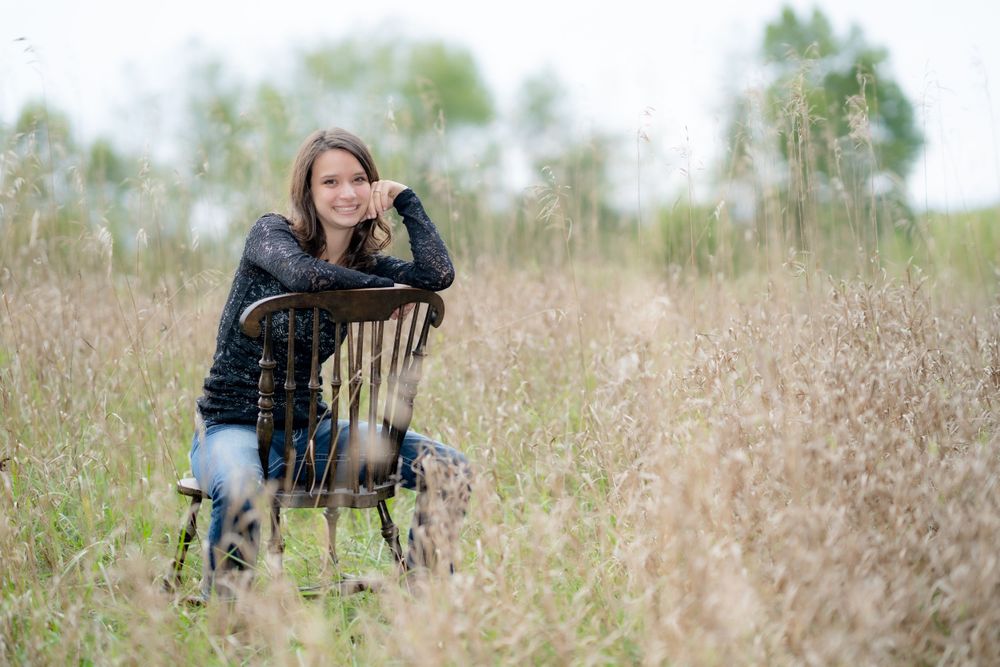 Woman in black top leans on chair in tall autumn grass field.