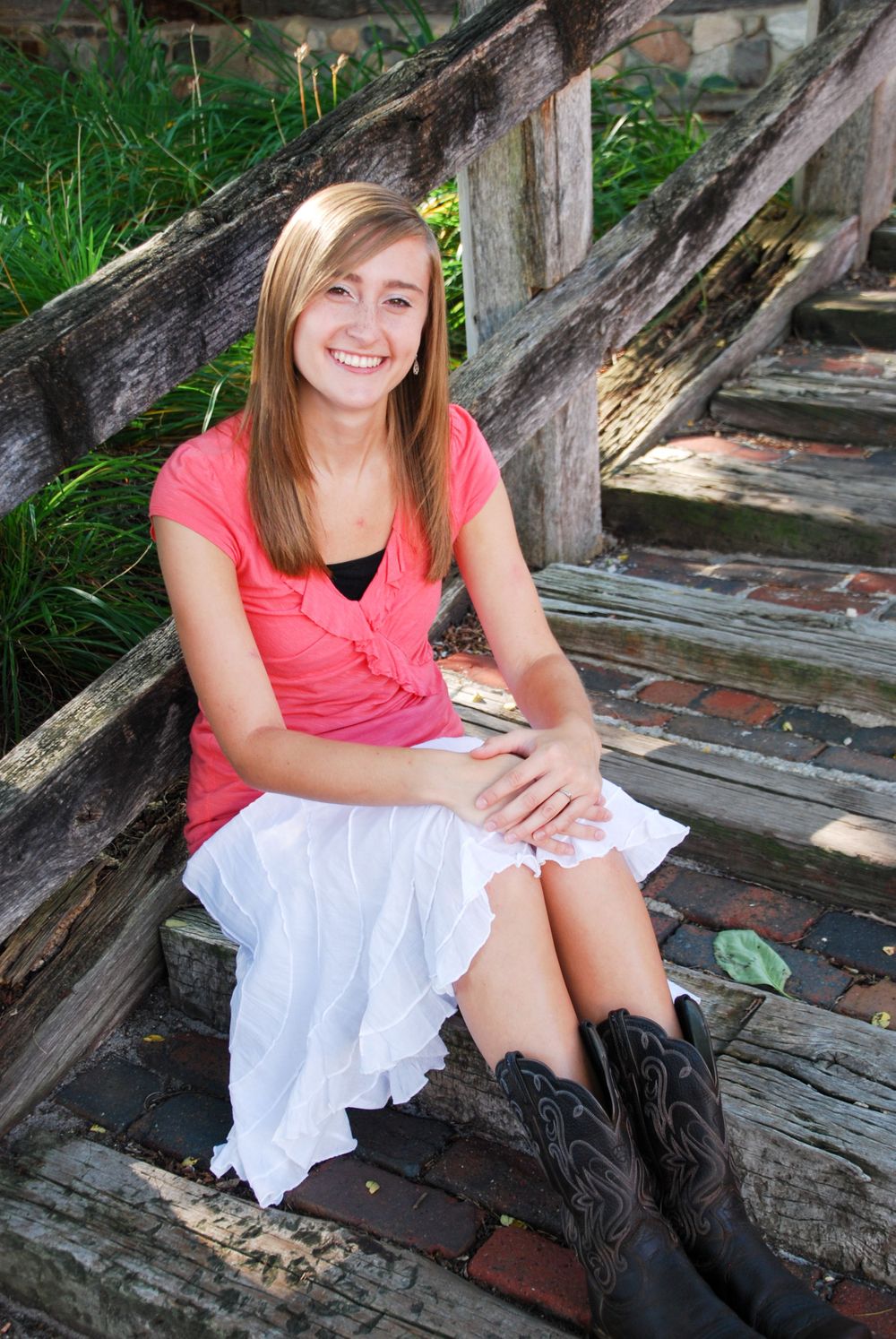 Person in coral top and white skirt sitting on rustic wooden steps outdoors.