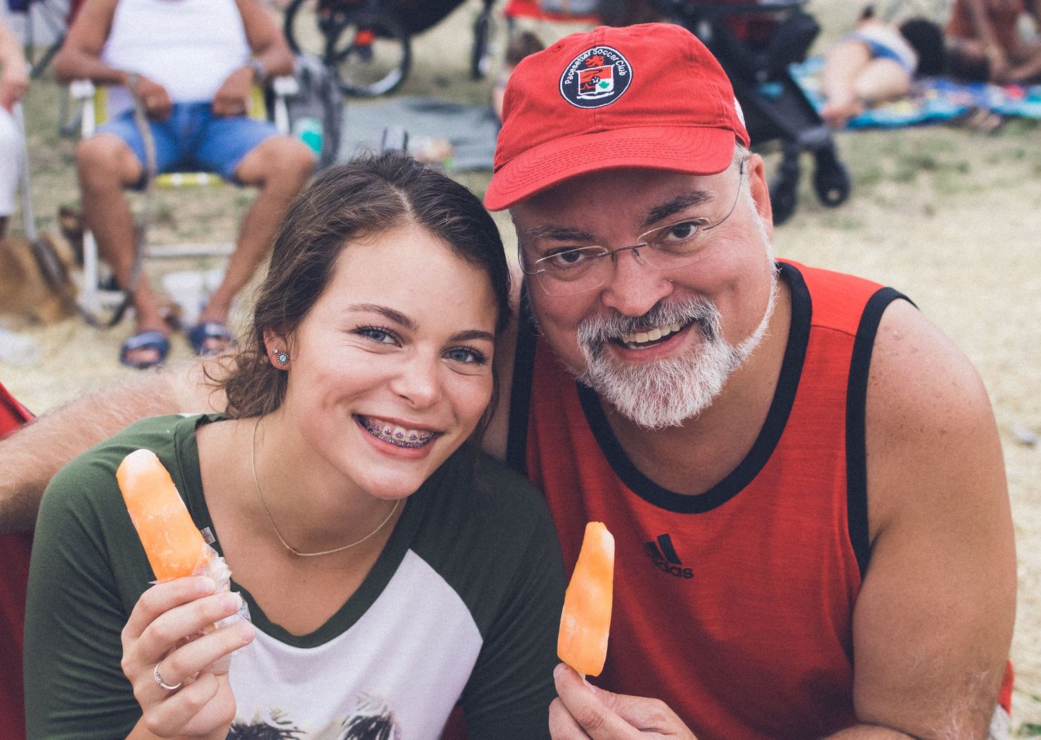 People enjoying outdoor festivities with red baseball caps and snacks.