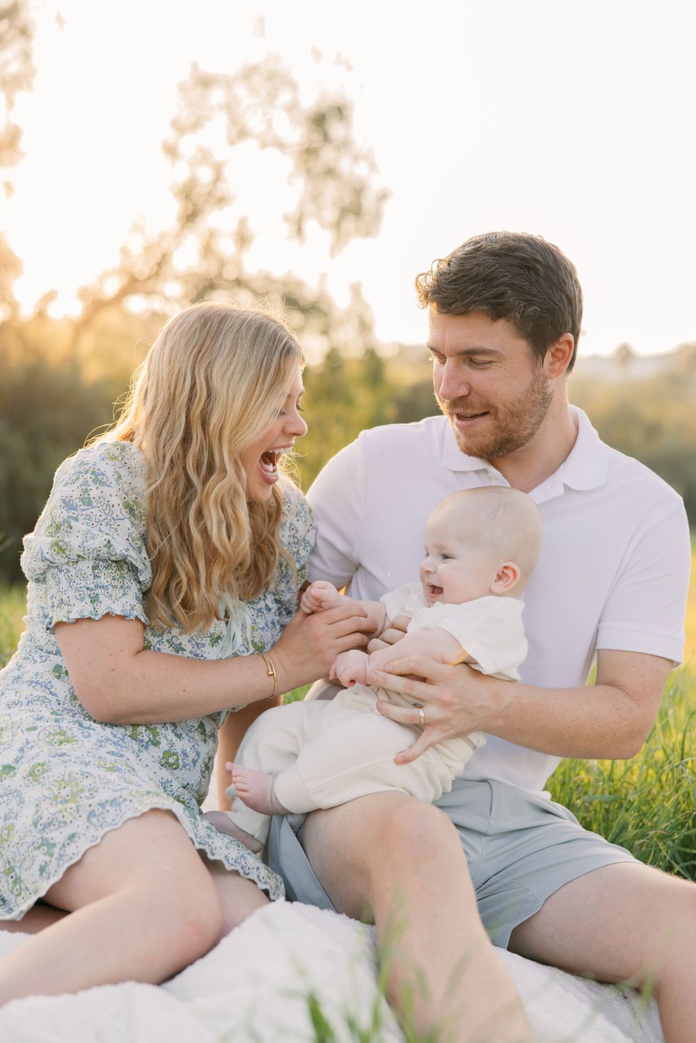 Couple playing with baby in grassy field during golden hour sunset.