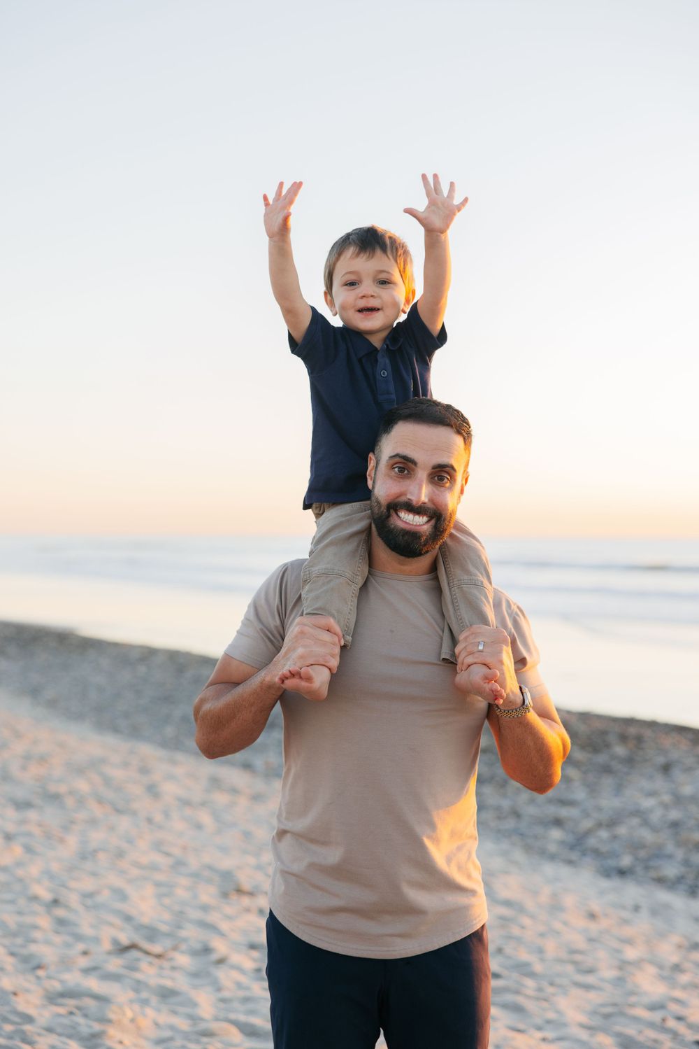 Joyful beach moment with child riding on shoulders during sunset.