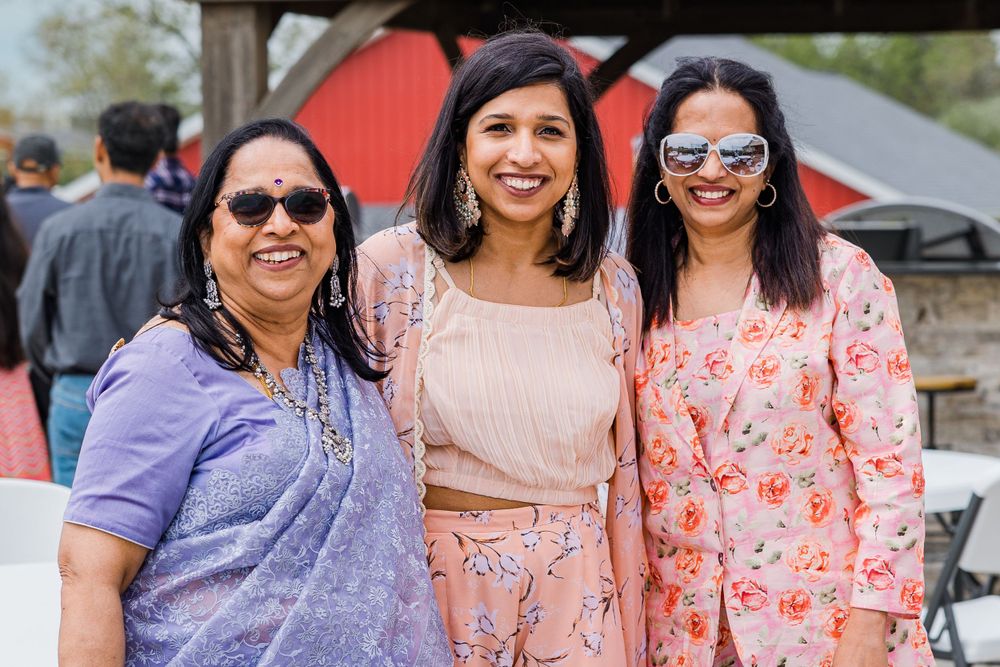 Three people in colorful traditional attire smiling together at an outdoor celebration.