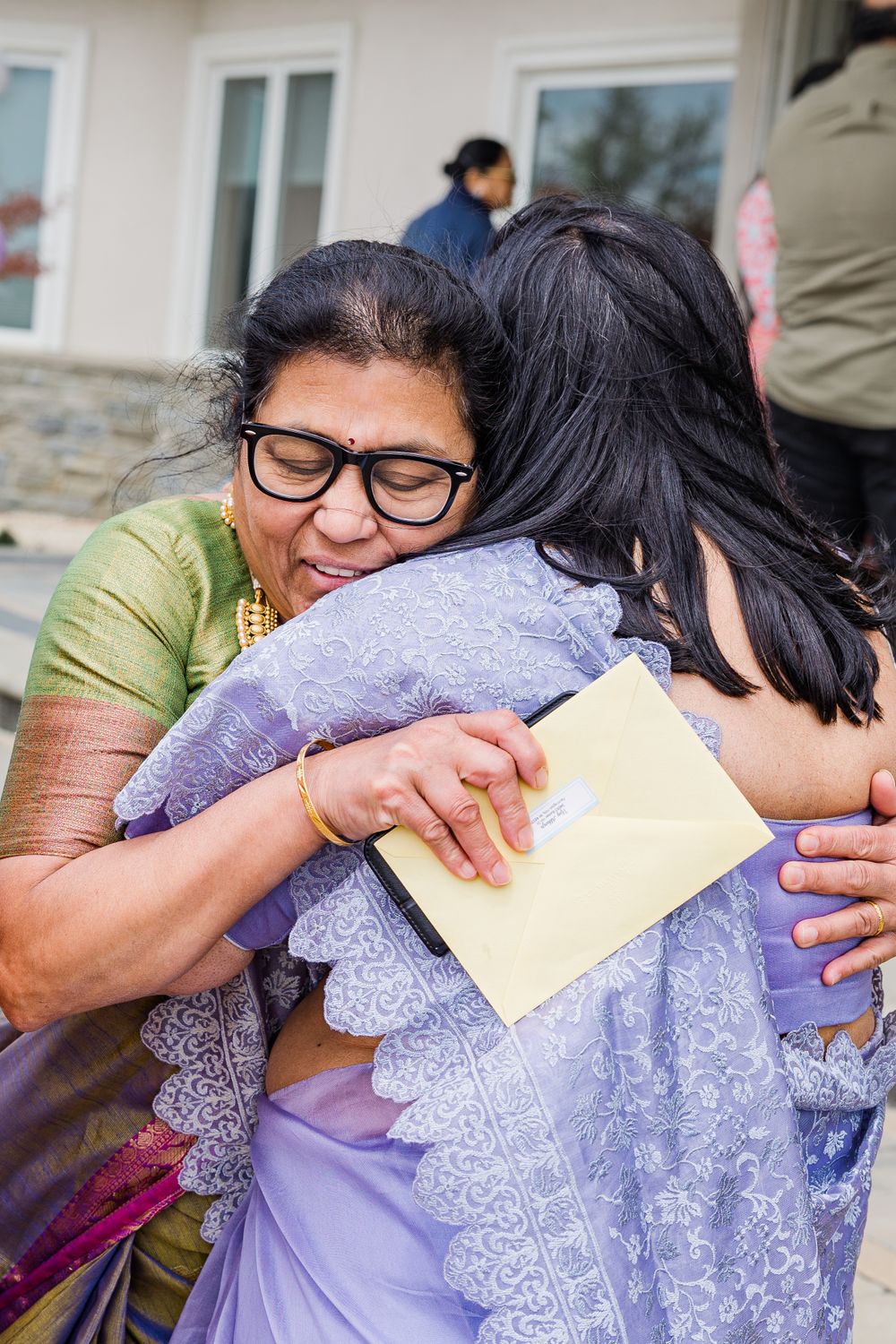 Two people sharing an emotional embrace while holding a document at an outdoor gathering.
