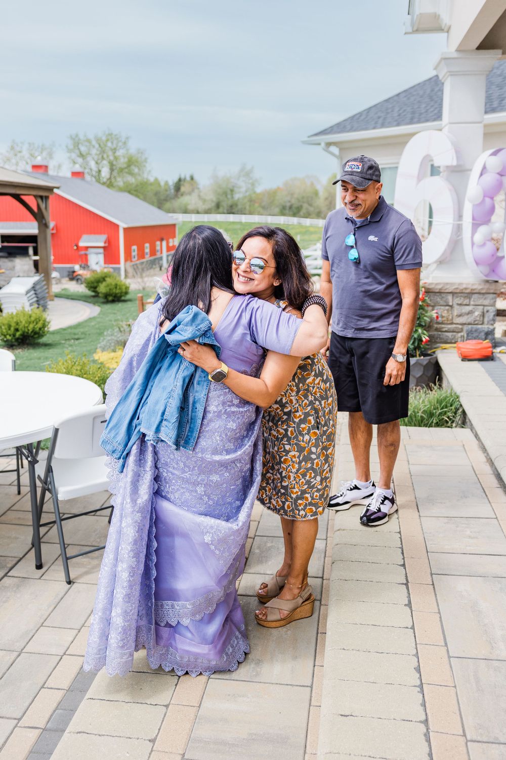 People sharing warm embraces at an outdoor celebration with a red barn in the background.