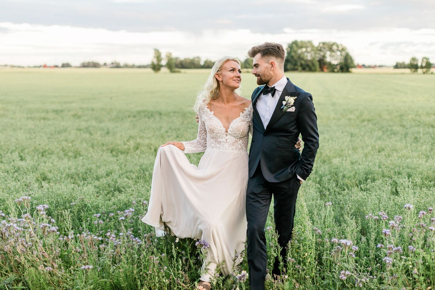 Joyful wedding couple walking together through a blooming meadow.