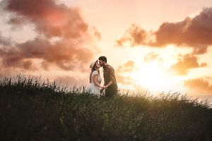 Romantic couple kissing on a grassy hill during a breathtaking golden sunset.