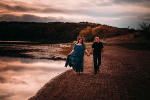 Couple walking hand in hand along lakeside path under dramatic cloudy sky.