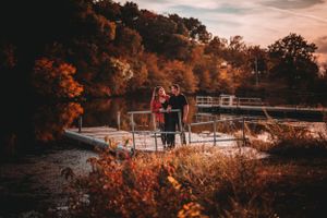 Couple standing on dock surrounded by colorful autumn foliage at sunset.