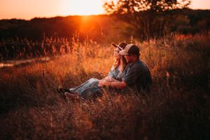 Couple sitting together in tall grass enjoying warm glowing autumn sunset.