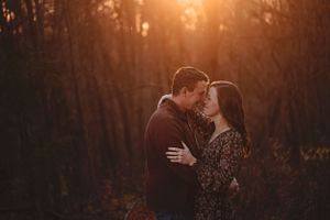 Couple sharing tender almost-kiss moment in sunlit autumn forest setting.