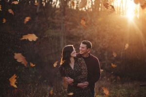 Happy couple laughing as golden leaves fall around them in autumn forest.