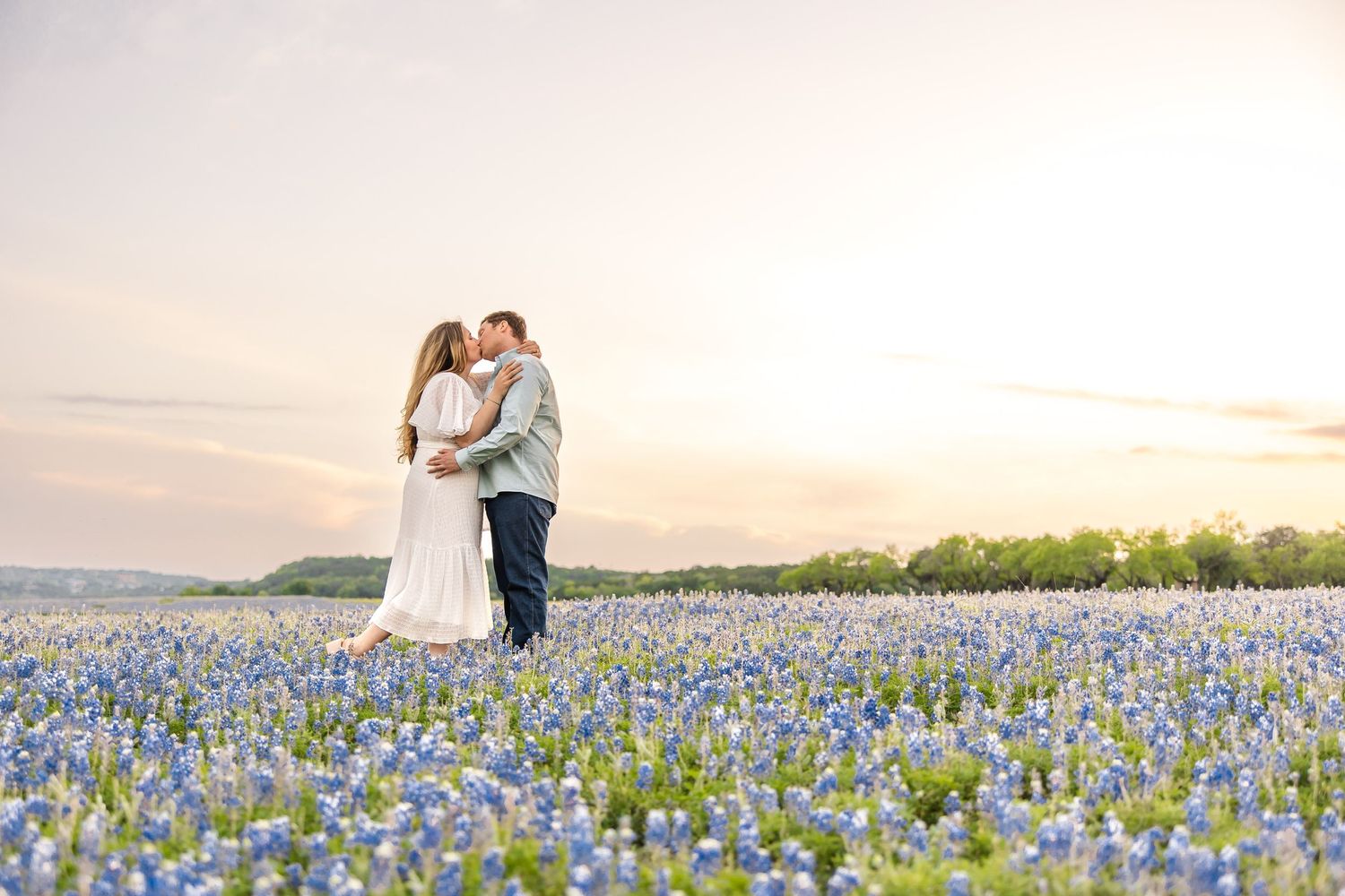 Couple embraces in field of blooming bluebonnets during sunset.