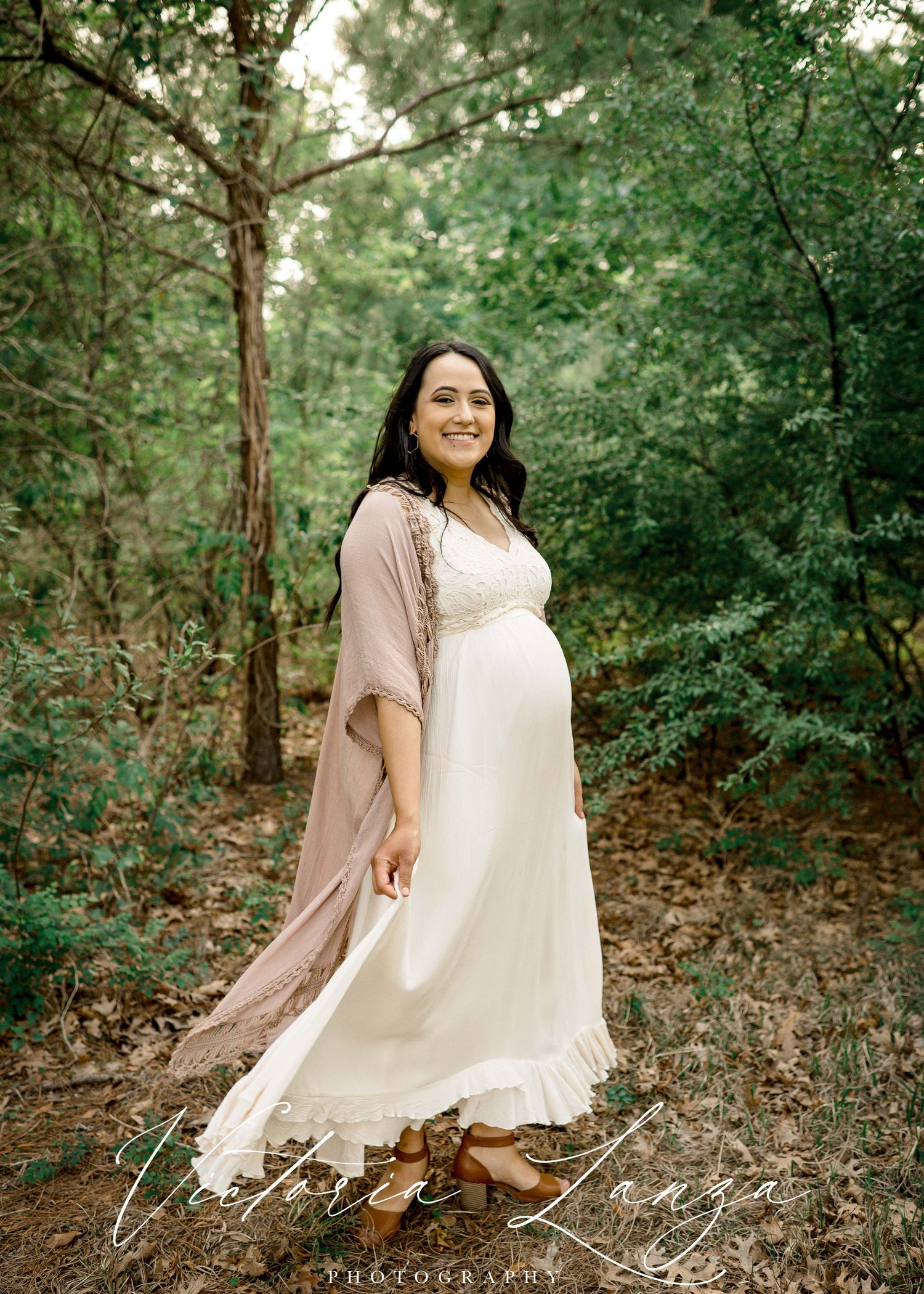 pregnant woman dancing in the trees smiling while taking portraits in houston texas while wearing a white lace dress
