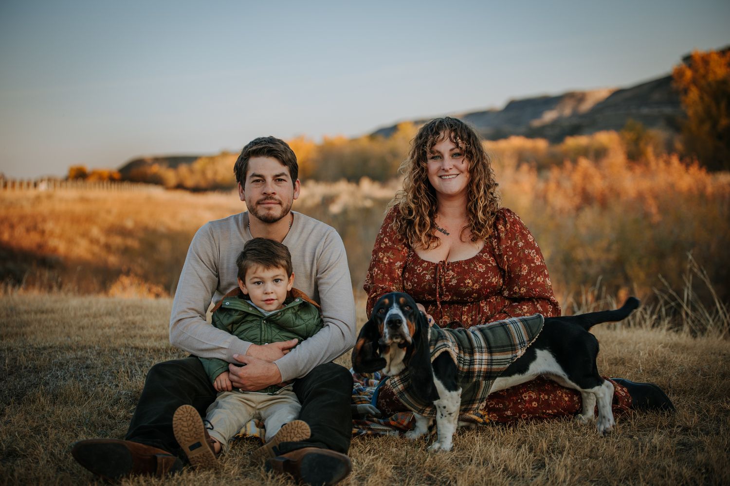 Family with dog enjoying golden hour in an autumn field with mountains in background.