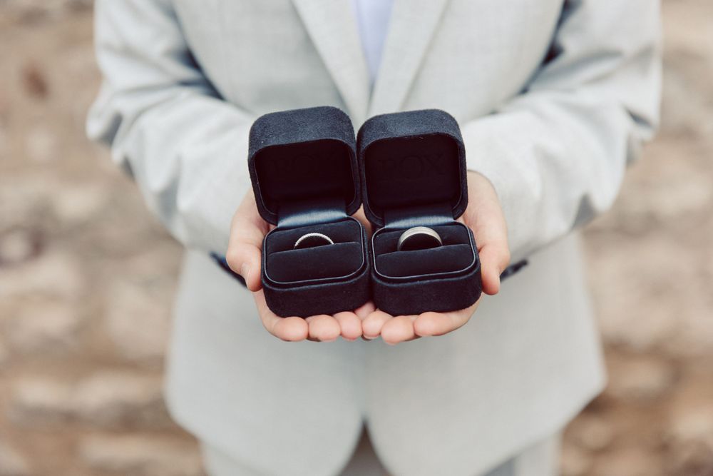 Hands holding multiple ring boxes against light colored background.